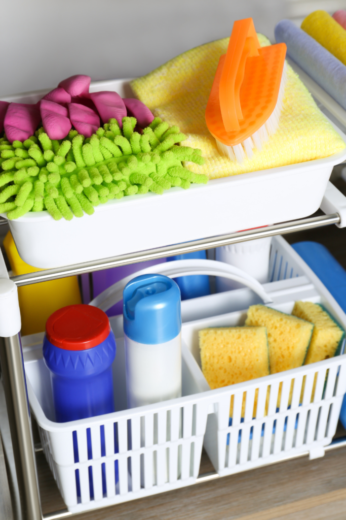 Pull-out cabinet organizer holding cleaning sprays, sponges, and brushes in kitchen cabinet