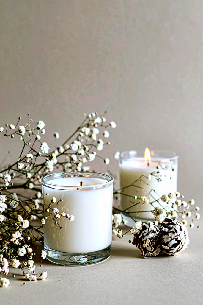 Set of three budget-friendly scented candles in neutral glass jars on a wooden tray, glowing softly in a cozy bedroom setting.