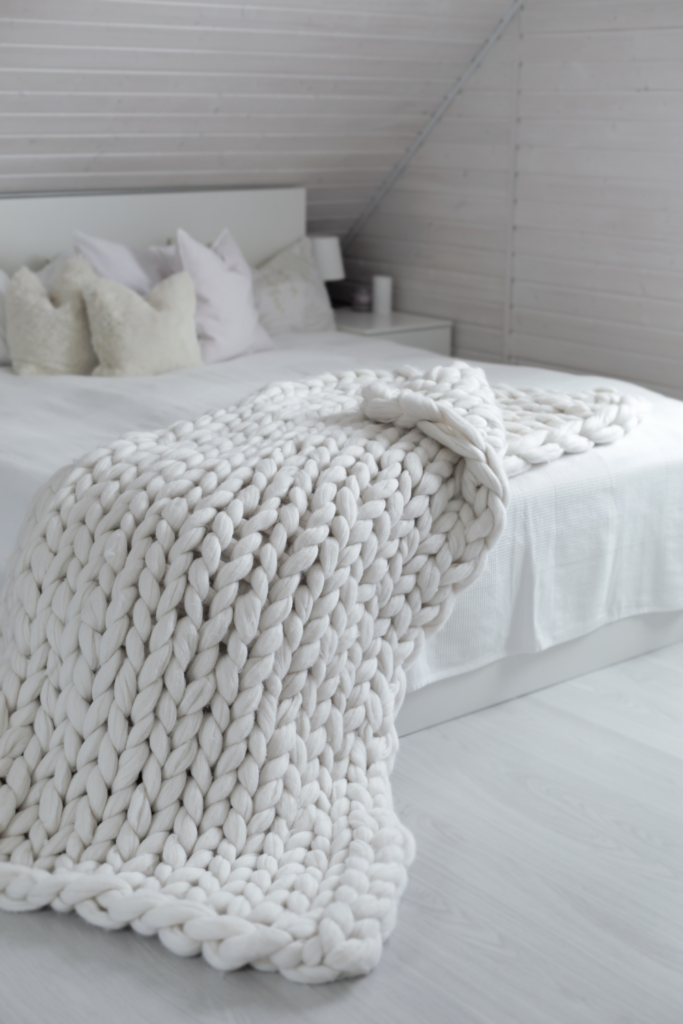 Soft neutral bedroom with layered white bedding and a cozy knit throw blanket draped across the end of the bed, creating a warm and inviting atmosphere.