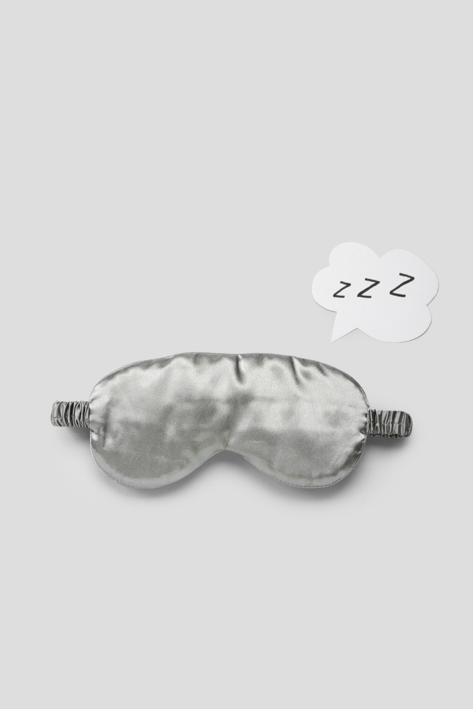 Soft, plush sleep mask in a neutral color resting on a cozy bedroom surface, designed to block light and enhance restful sleep for under $50.