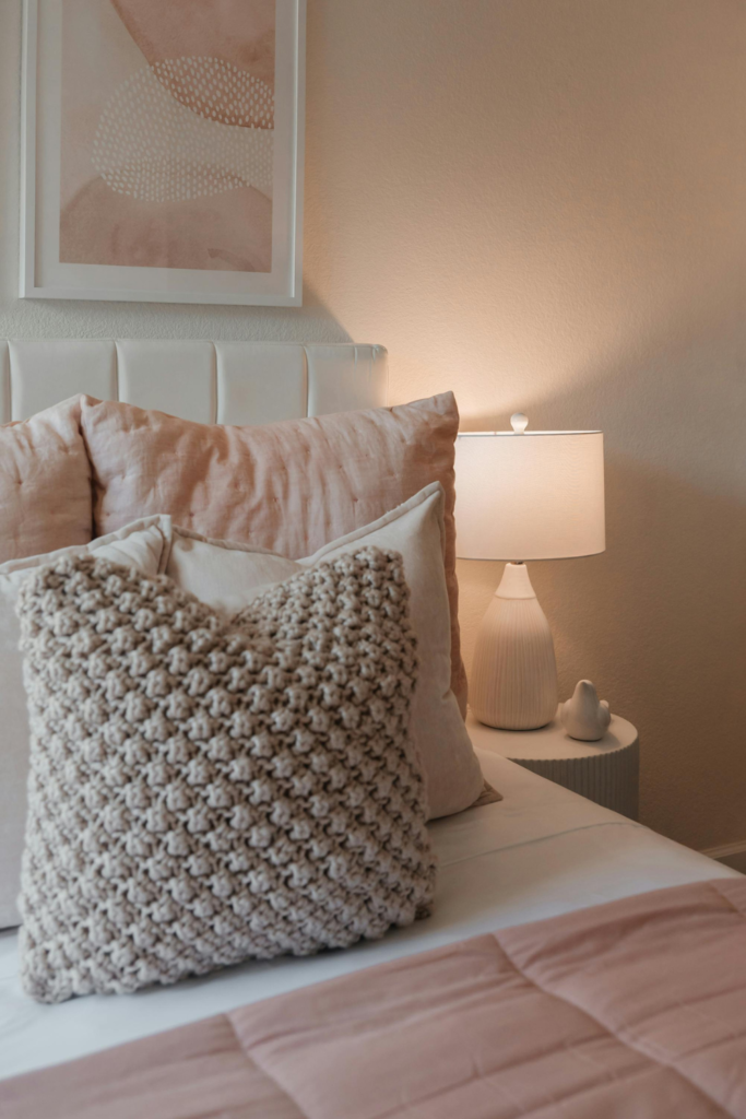 Plush faux fur pillow in a soft neutral color layered on a bed with white and pink bedding, adding cozy texture and warmth to the bedroom for under $50.