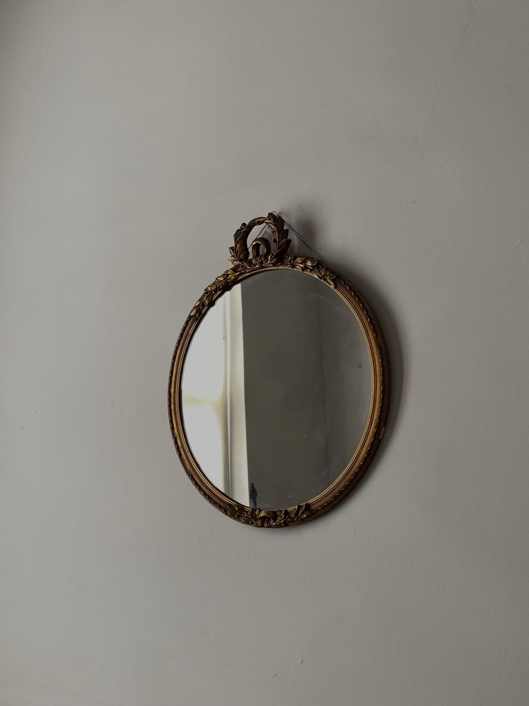 A classic round mirror with ornate frame reflecting a soft light on a plain wall.