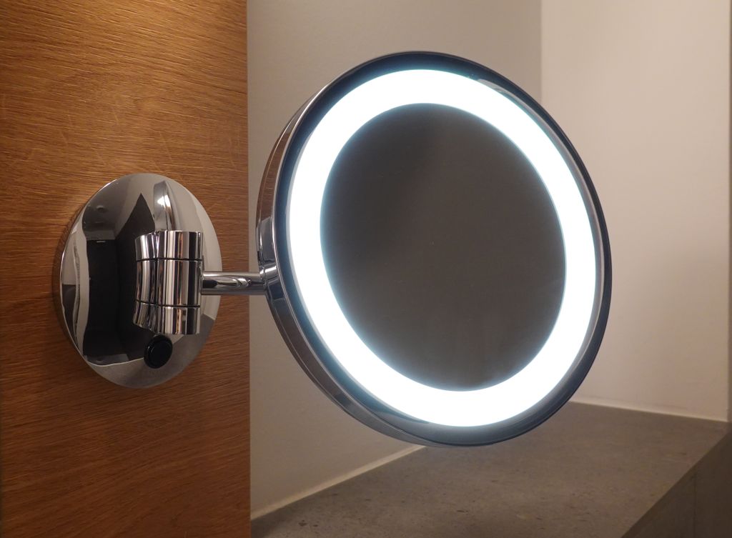 Close-up of a contemporary chrome makeup mirror with LED light, in a modern bathroom setting.